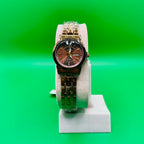 Gold watch on a white stand against a green background