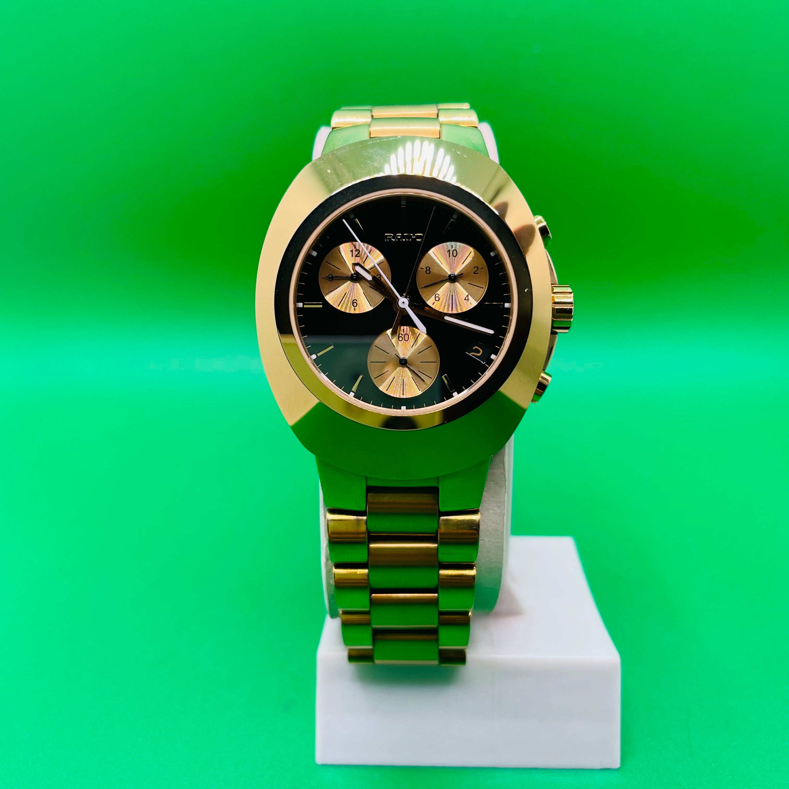 Gold wristwatch on a white stand against a green gradient background